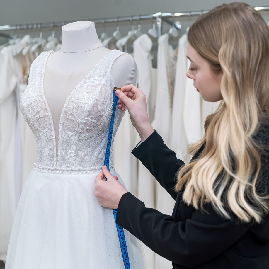 charming-woman-saleswoman-stylish-black-suit-measures-wedding-dress-with-measuring-tape